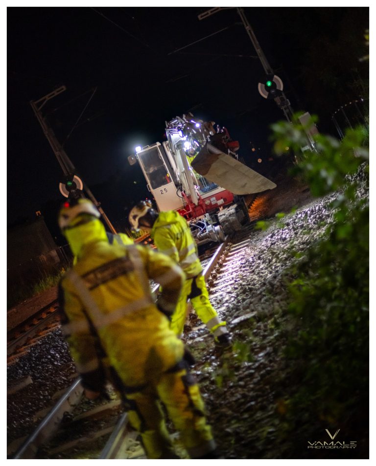 Grävmaskin på spåret i nattmiljö, arbetsplats med starkt ljus och industriell känsla - Vamale Photography