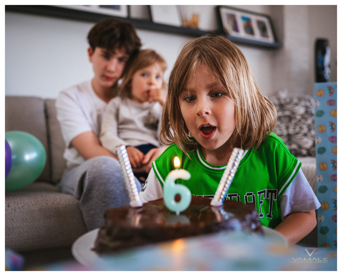 Barn blåser ljus med bröder i bakgrunden Barn som blåser ut ljus på födelsedagen med sina bröder i bakgrunden, fångat i ett varmt familjeögonblick. Foto - Vamale Photography
